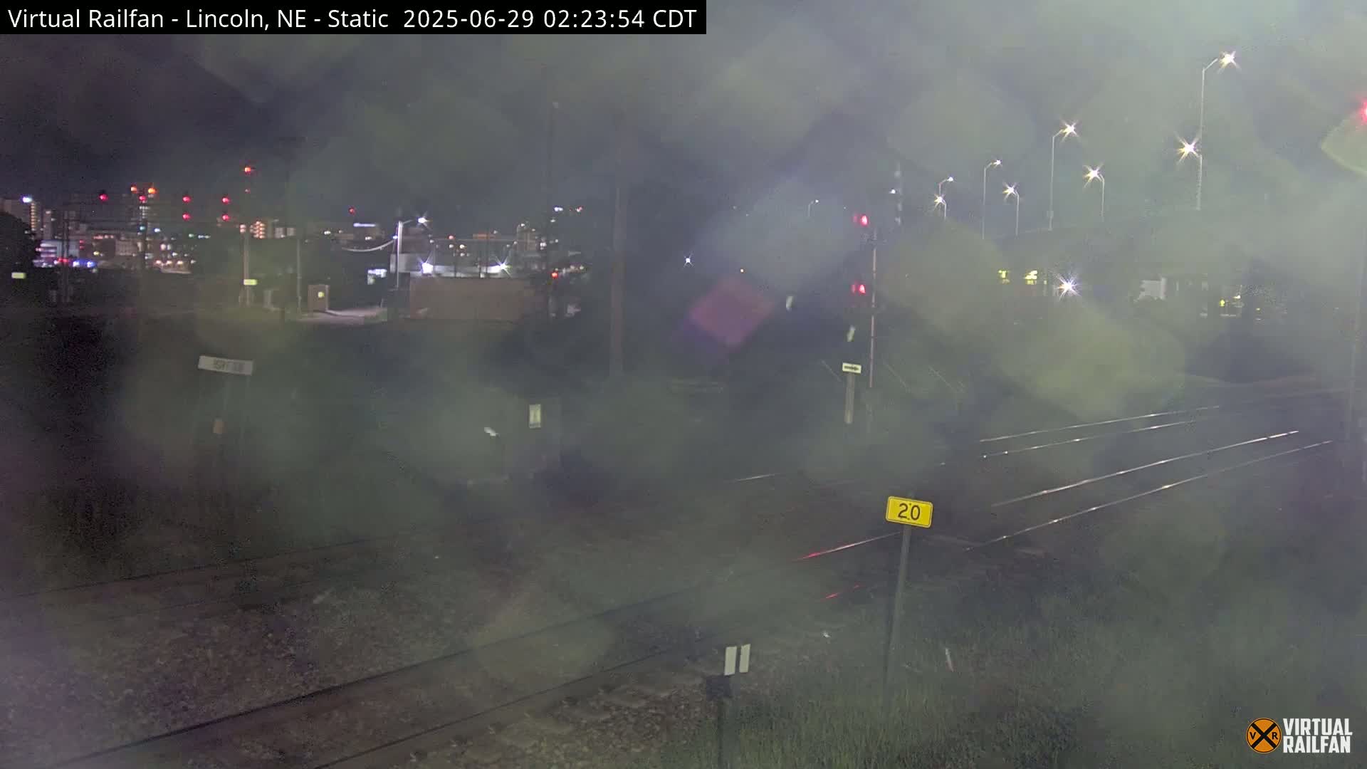 A nighttime view of railroad tracks near a city, obscured by a hazy atmosphere.