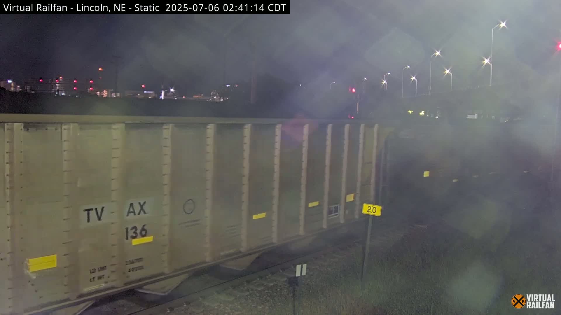 A tan railcar sits on tracks at night under hazy, dim lighting.