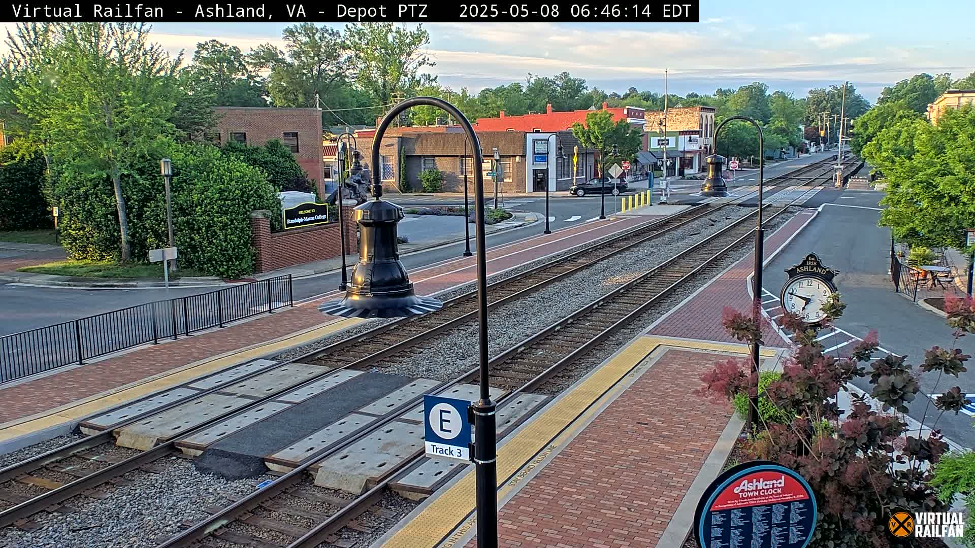 A train track runs through a brick-paved town square on a partly sunny morning.