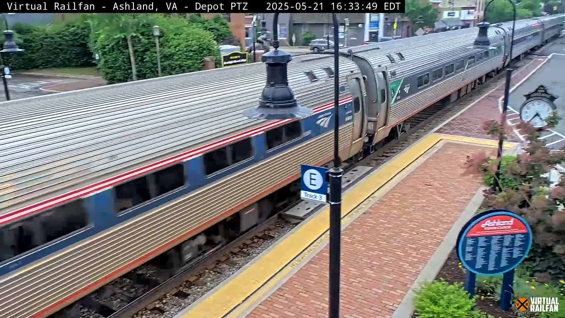 A long passenger train departs a station on a partly cloudy day.