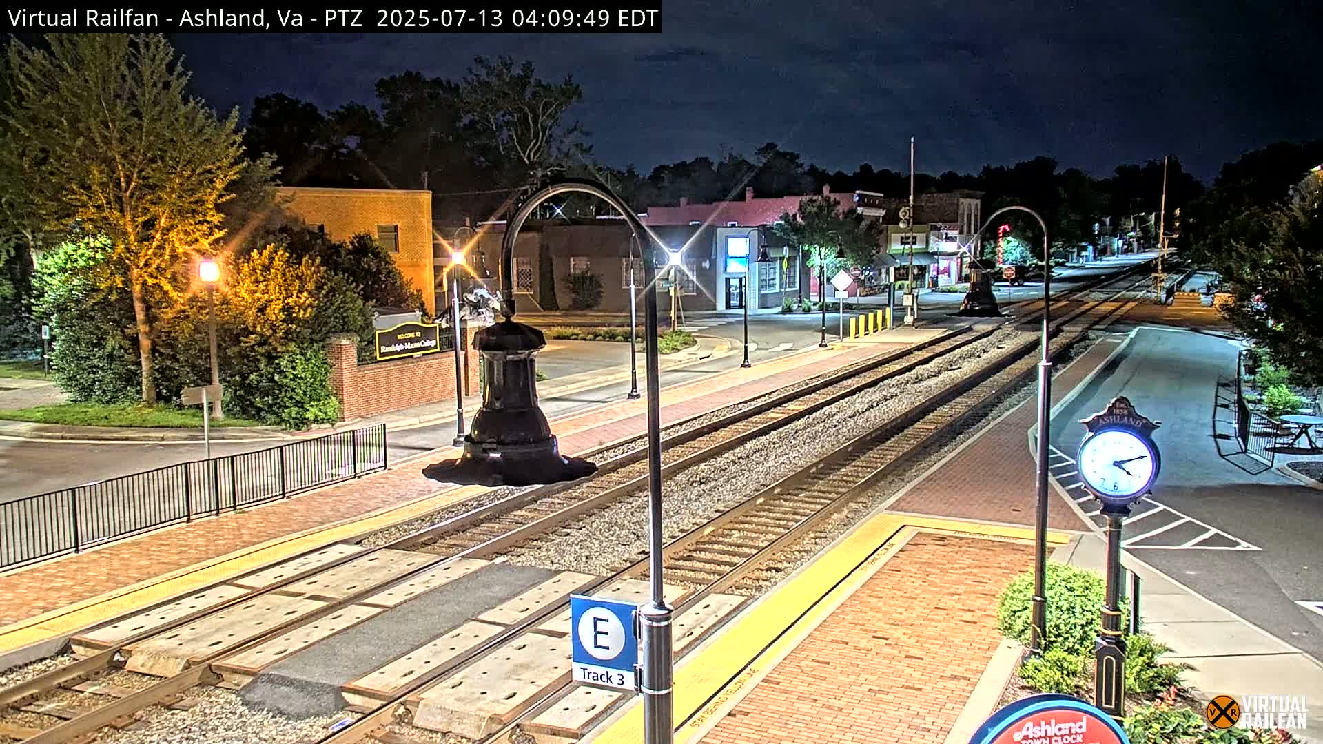 A nighttime view of a train track in a town, with streetlights illuminating buildings and a clock.