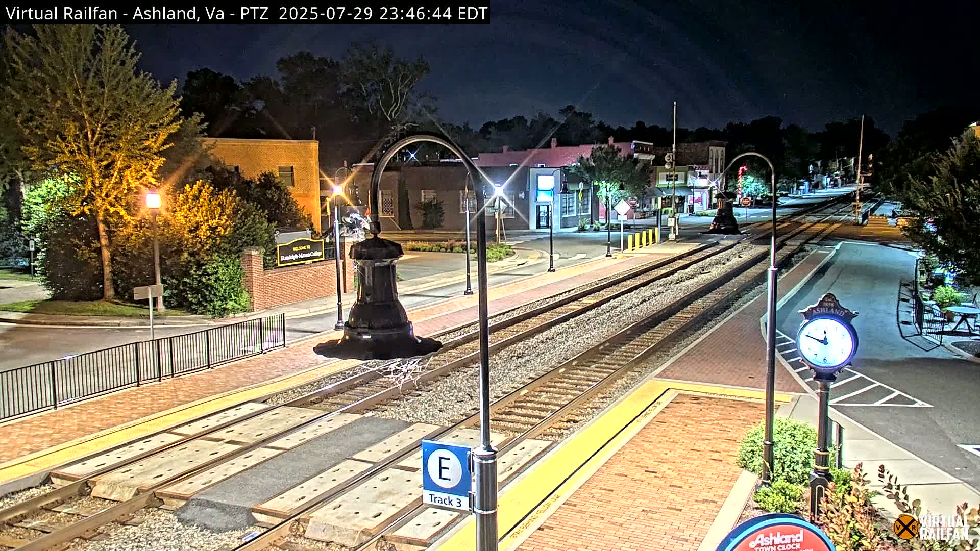 A nighttime view of a train track in a town, with streetlights illuminating buildings and a clock.