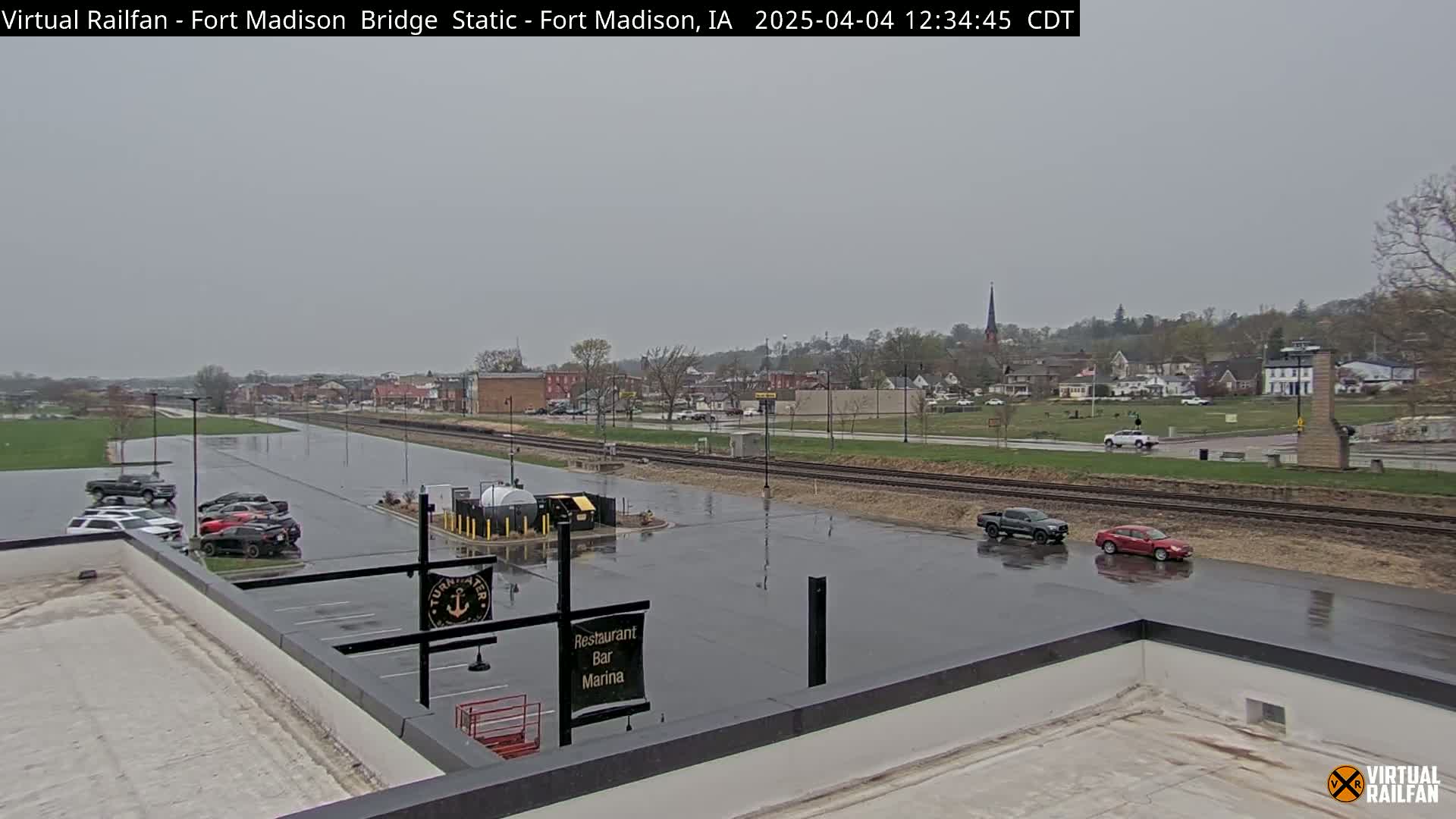 A wet parking lot and a small town are visible under an overcast sky.