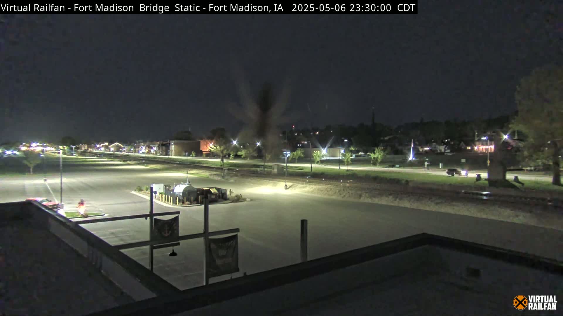 A nighttime, mostly clear view of an empty parking lot, a road, and a town in the distance.