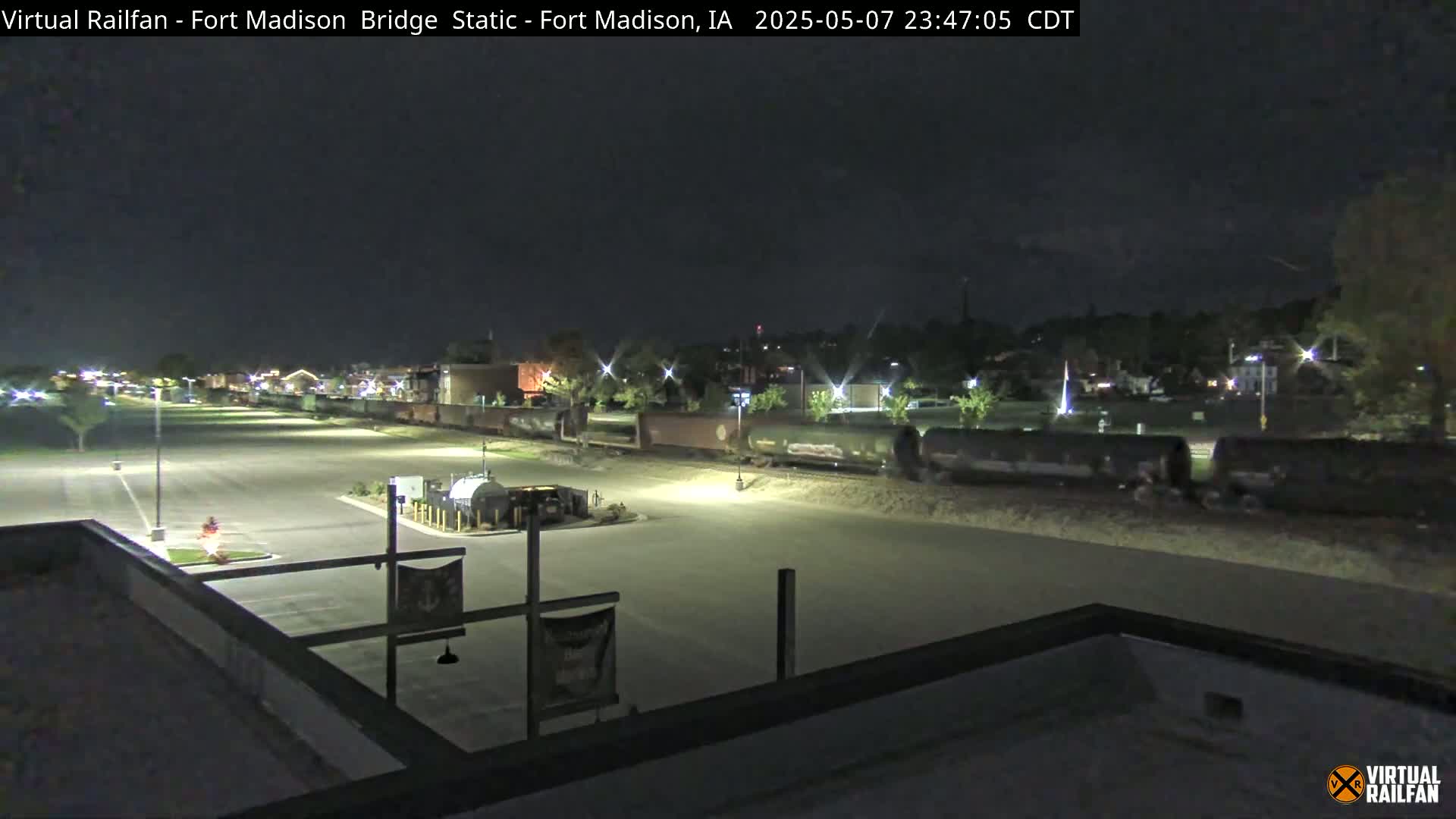 A long freight train is parked at night in a mostly empty parking lot, under a dark sky.