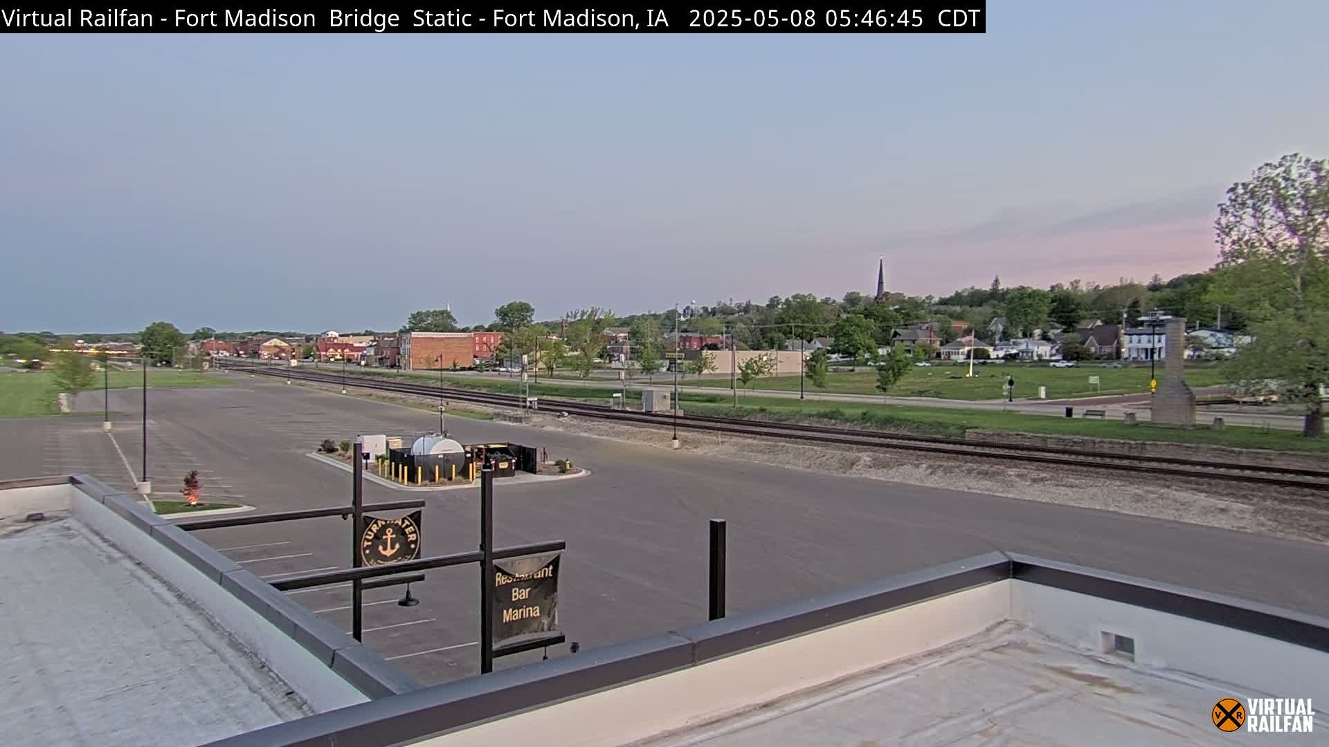 A mostly empty parking lot overlooks a small town with a railroad track in the foreground, under a twilight sky.
