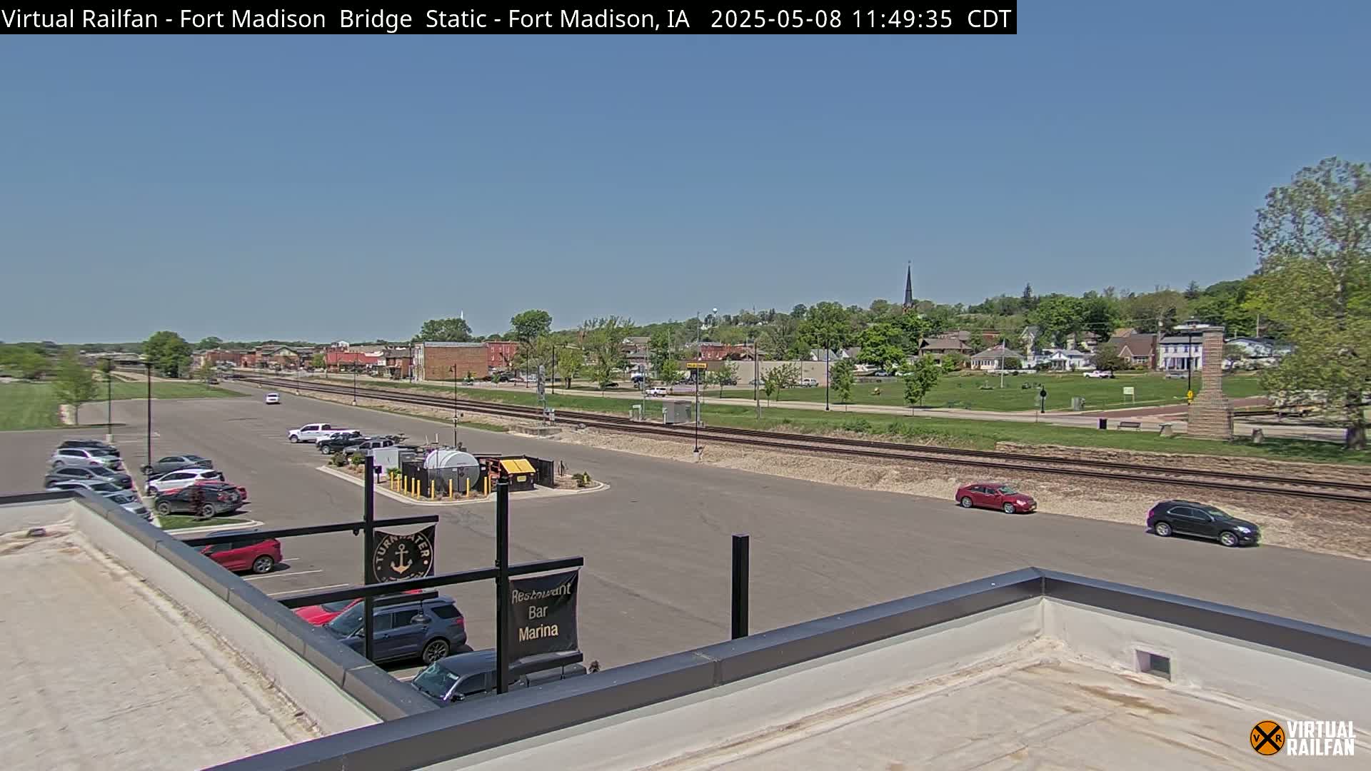 A small town is visible under a clear blue sky, with a parking lot, railroad tracks, and a few cars in view.