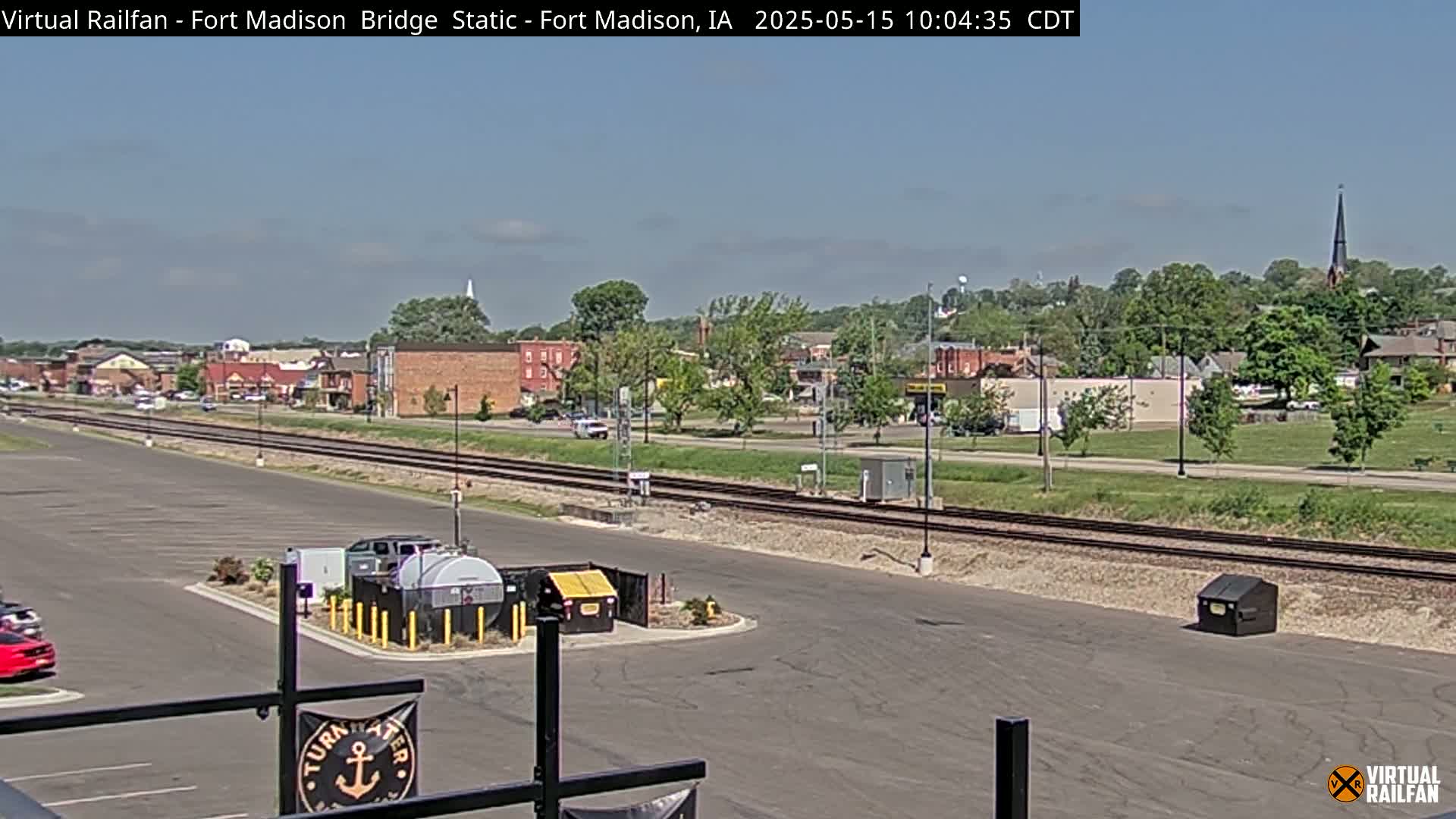 A parking lot and railroad tracks are seen in front of a small town on a partly sunny day.