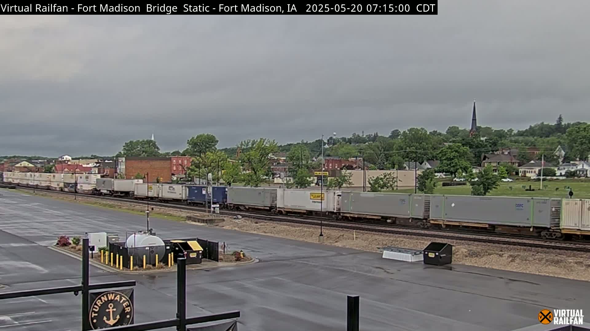 A long freight train passes through a town under an overcast sky.