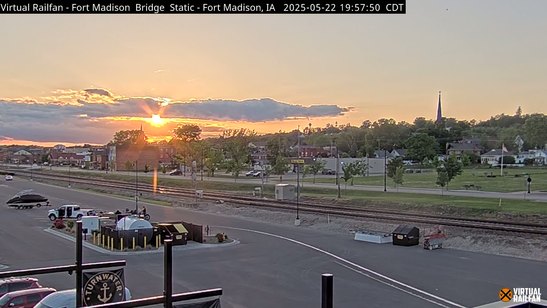 A sunset over a town with a train track, parked vehicles, and equipment in a parking lot.