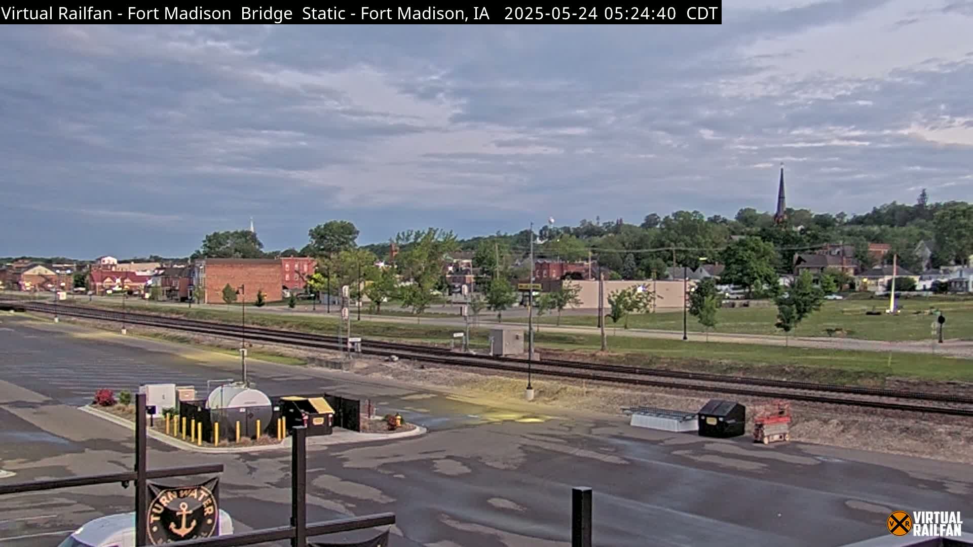 A mostly cloudy morning view of a small town with railroad tracks in the foreground and a parking lot with some equipment.