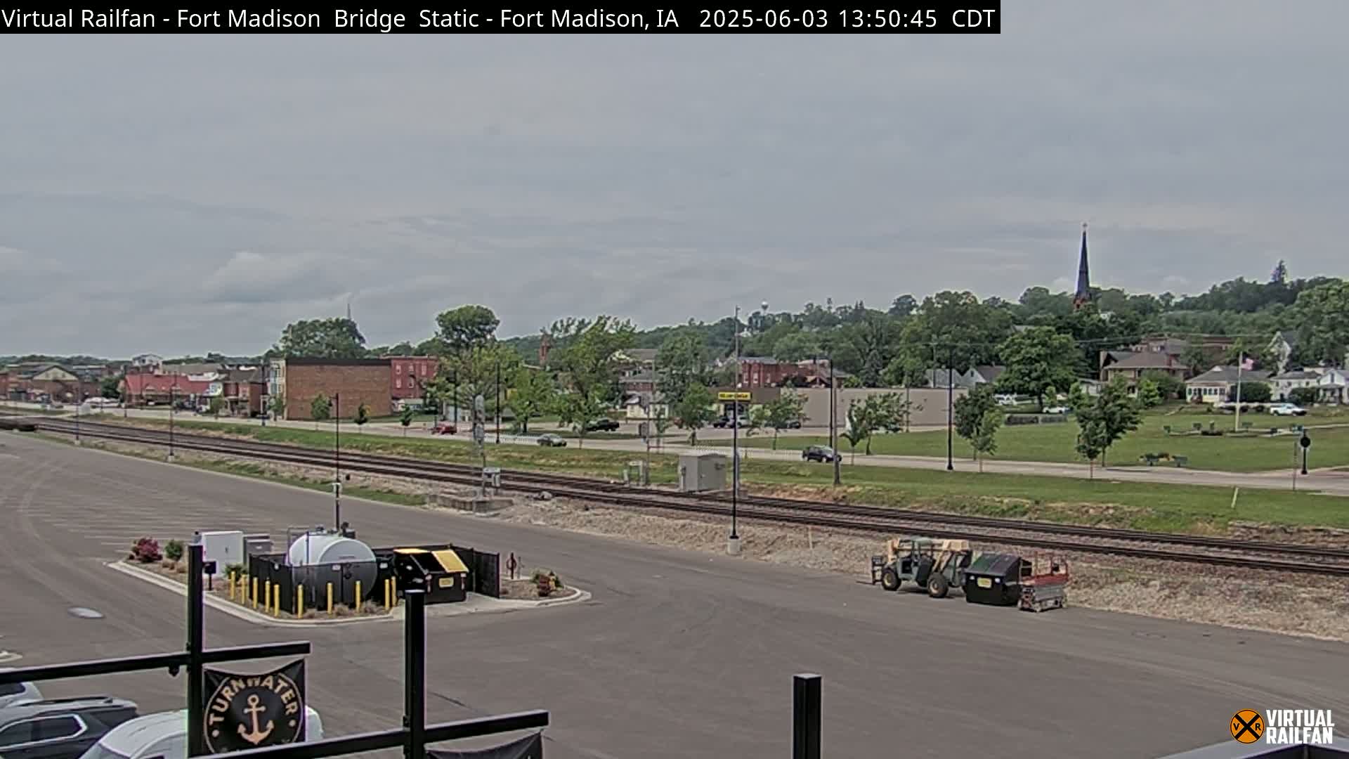 A view of a town under a cloudy sky, showing railroad tracks, a parking lot, and some small pieces of construction equipment.