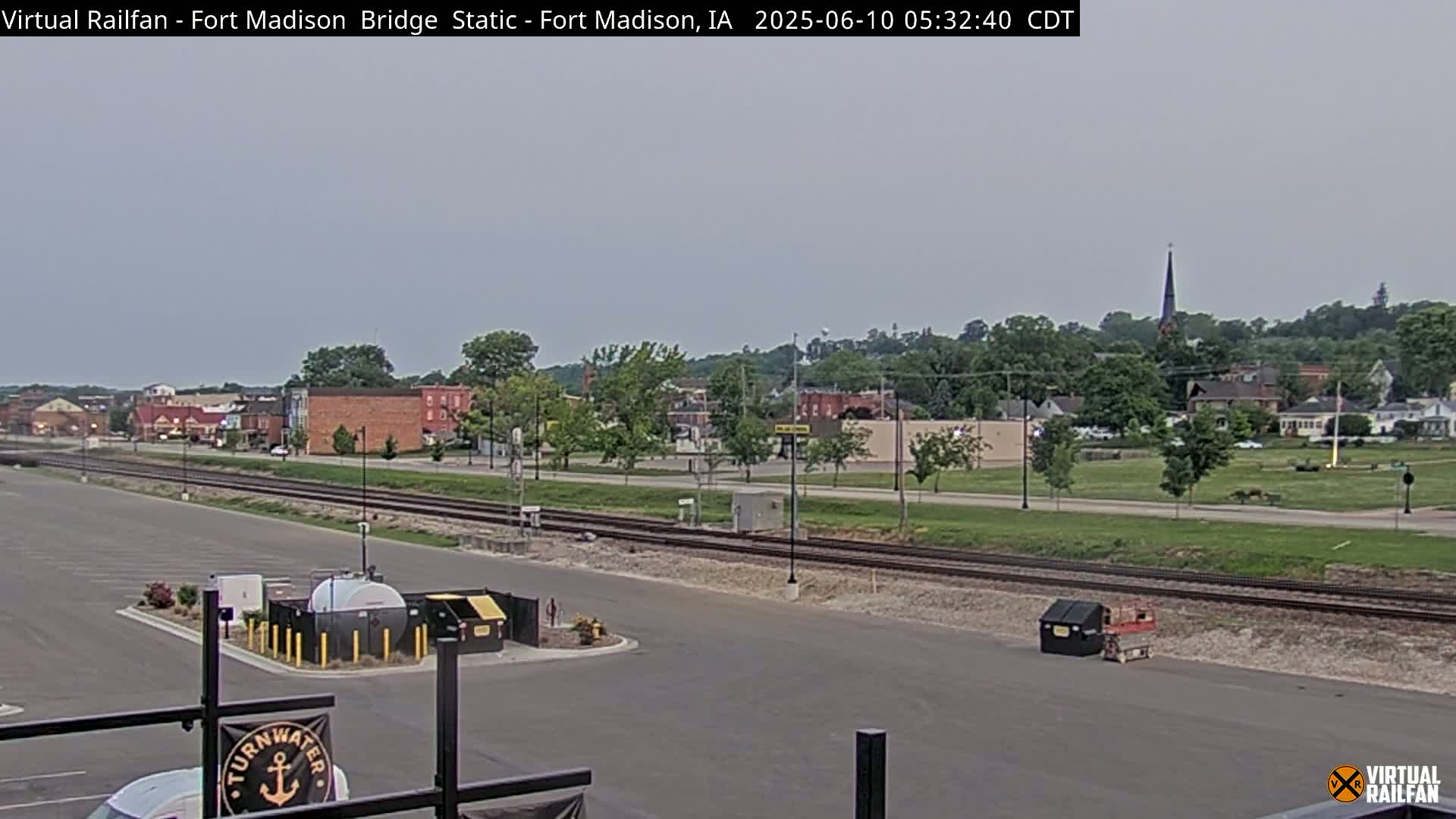 A mostly clear, overcast sky overlooks a town with railroad tracks running through the foreground and a parking lot with various equipment in it.