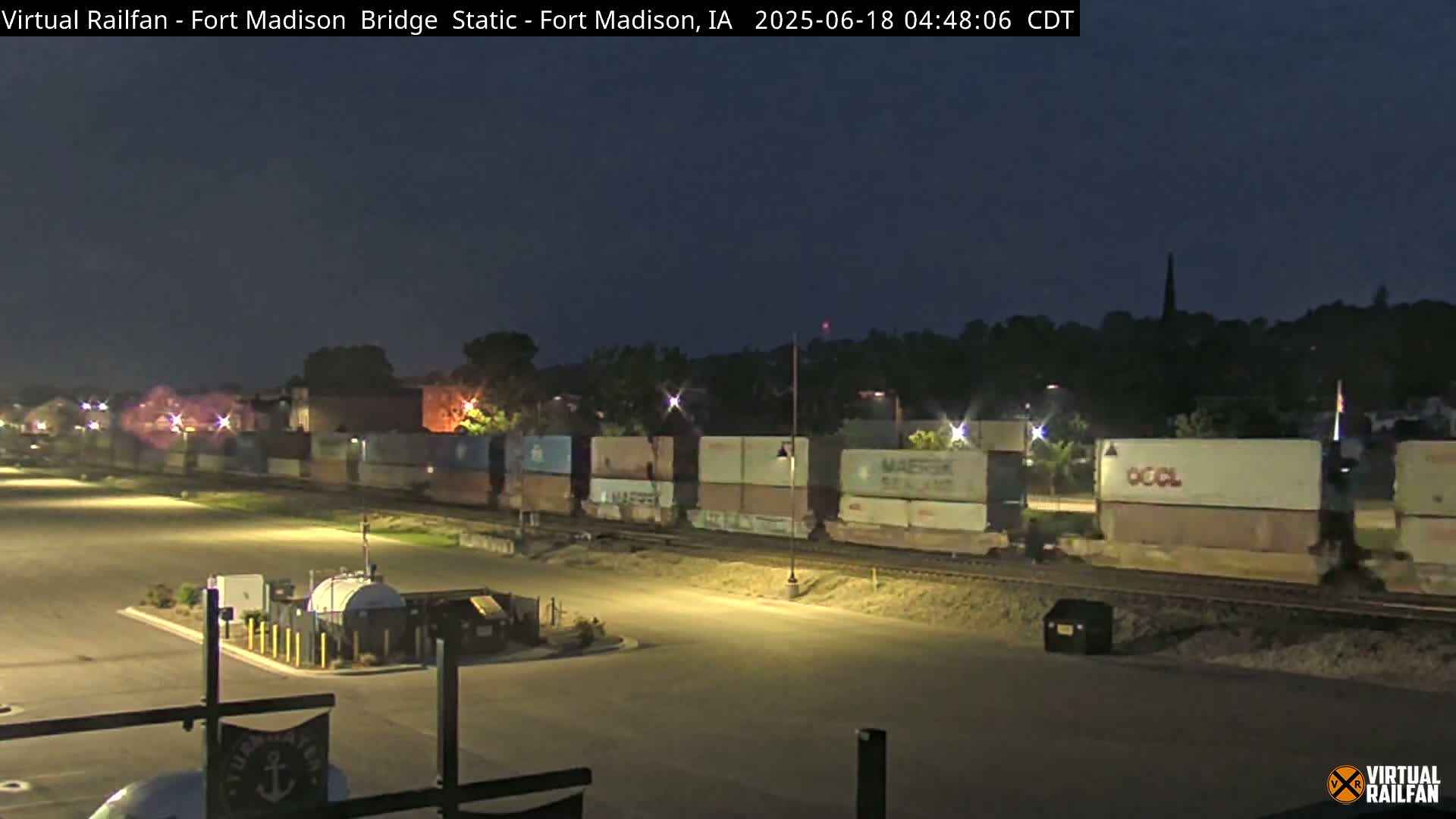 A long train of cargo containers sits on railroad tracks at night under a dark sky.