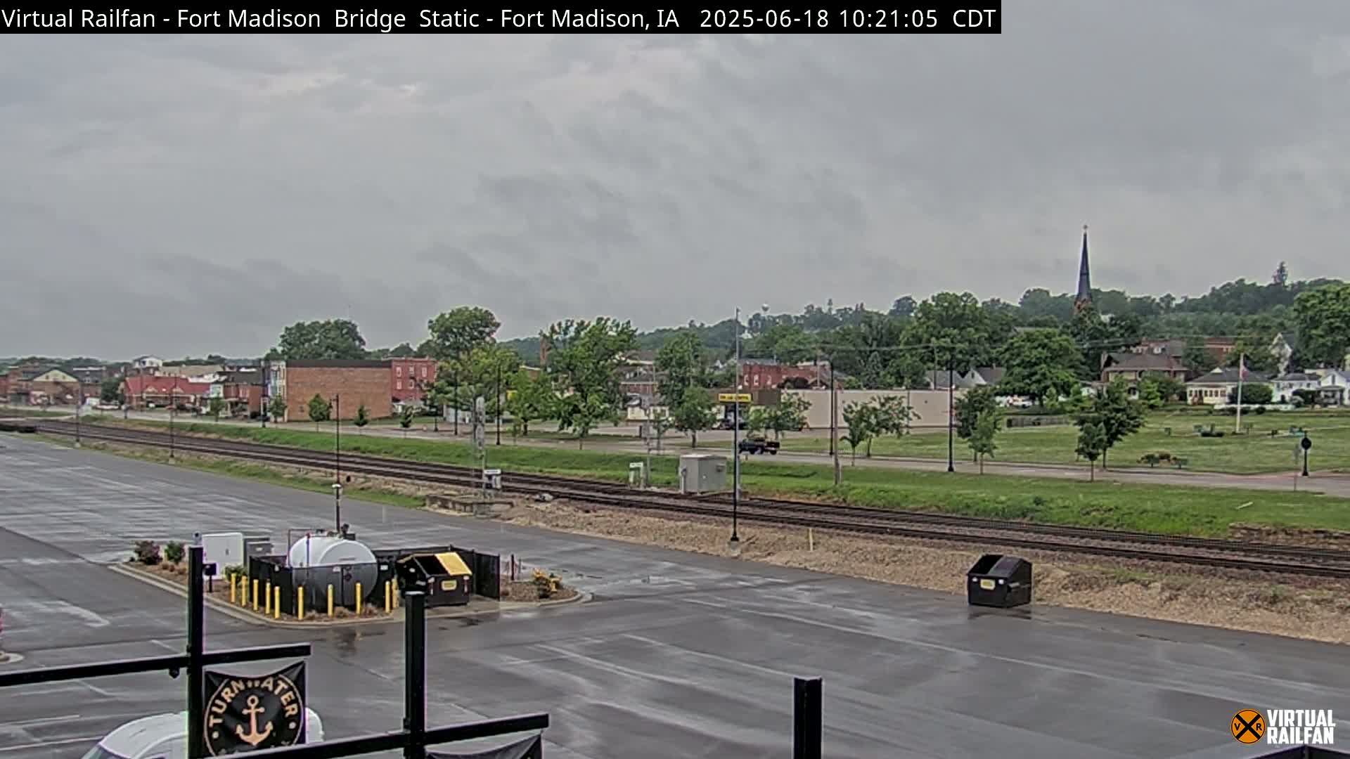 A wet, overcast view of a town with railroad tracks in the foreground, and a church steeple visible in the distance.
