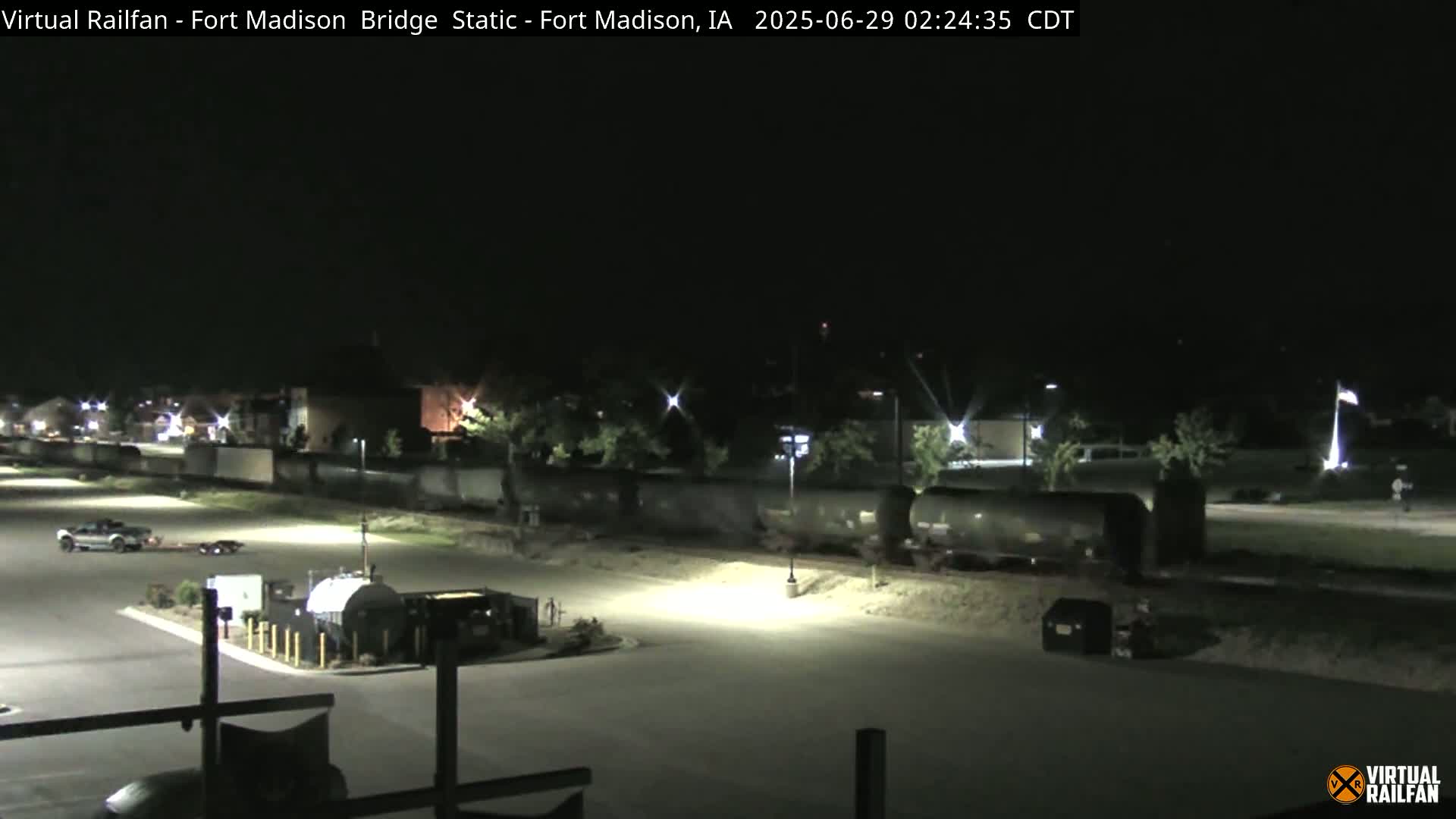 A nighttime view of a parking lot with a long freight train parked nearby, illuminated by artificial lights.