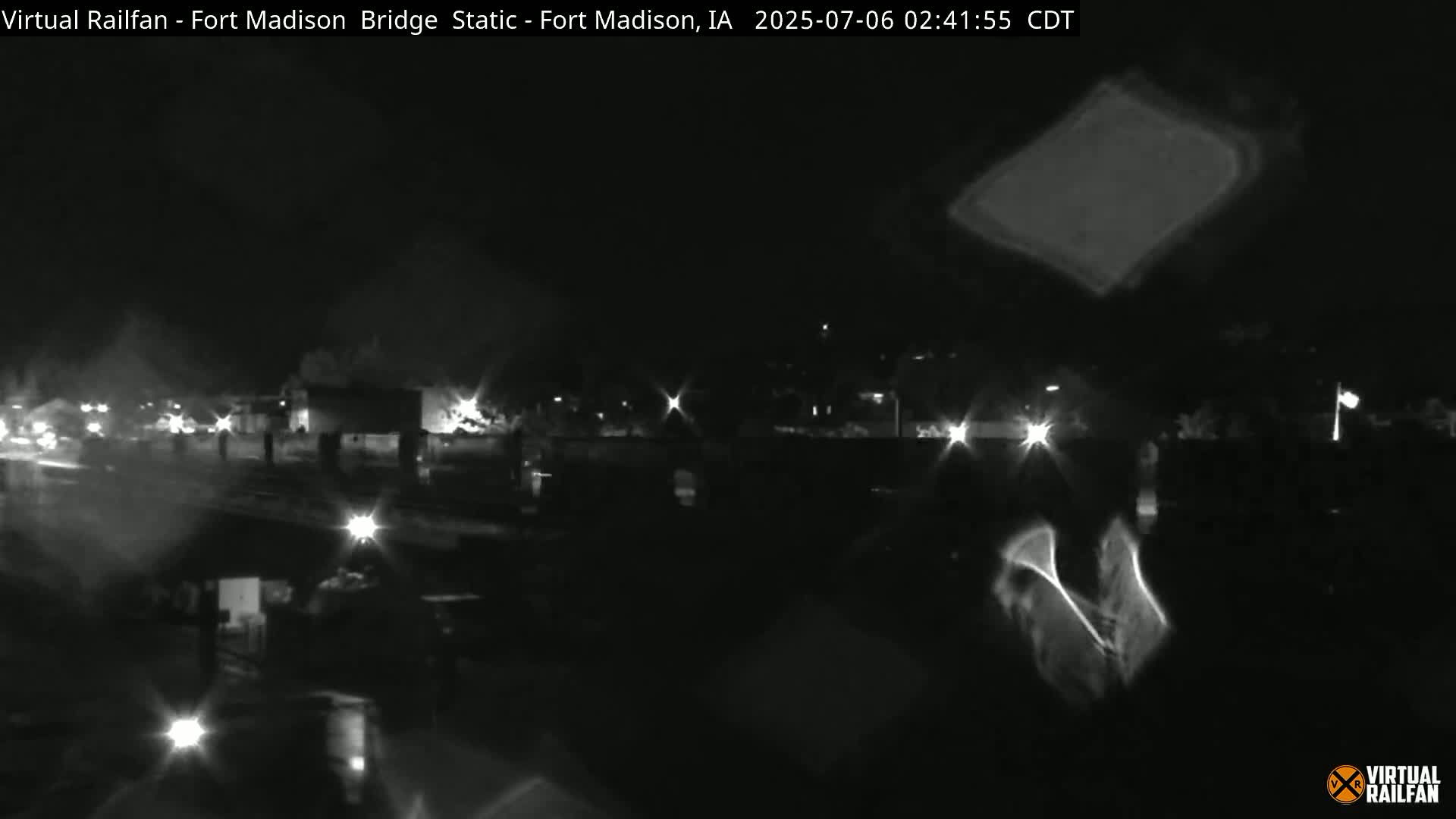 A nighttime, low-light view of a bridge and surrounding area, possibly featuring some light rain or moisture on the lens.