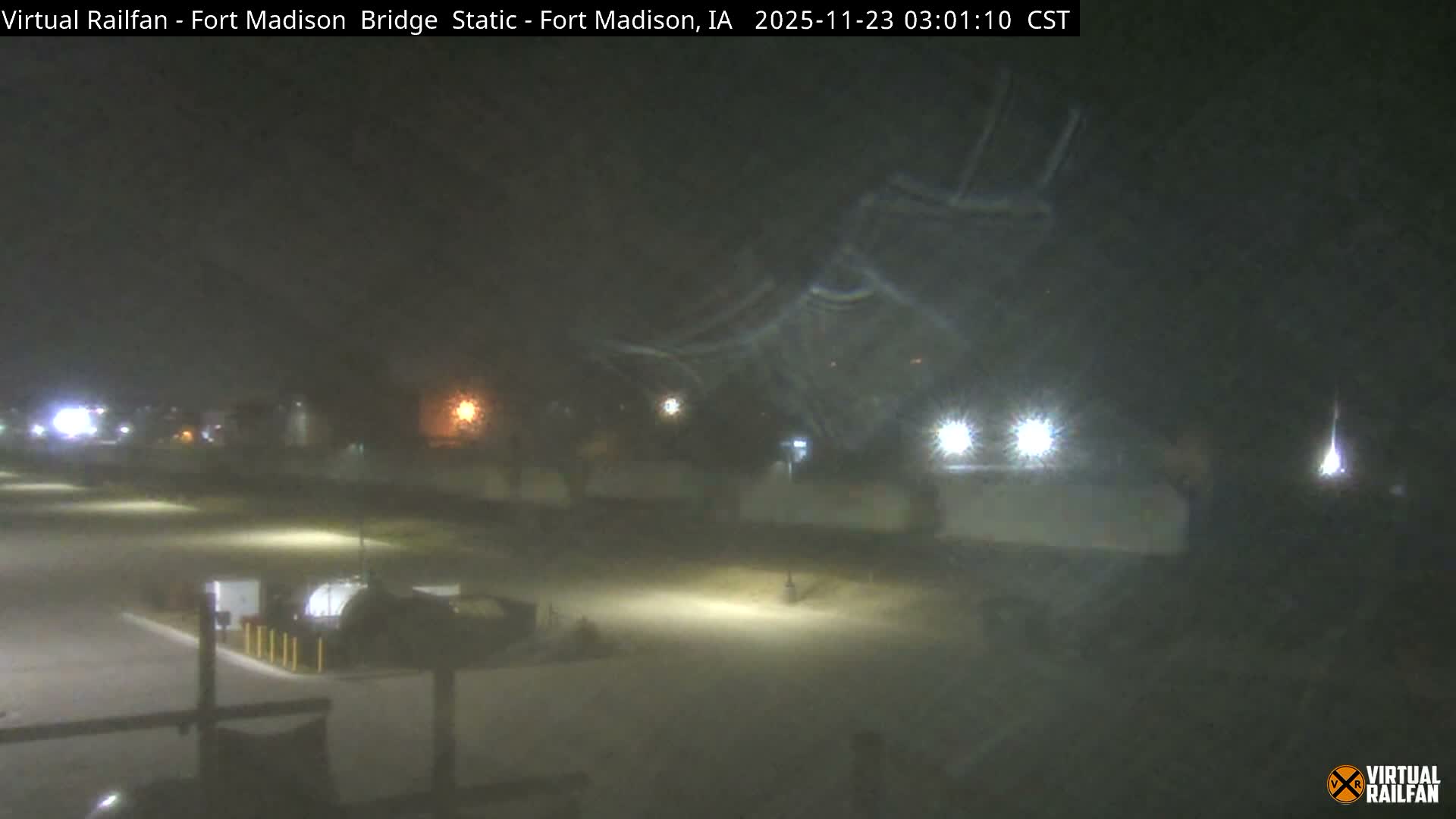 A hazy outdoor scene at night with reduced visibility, likely due to widespread fog or mist, illuminated by numerous bright lights.