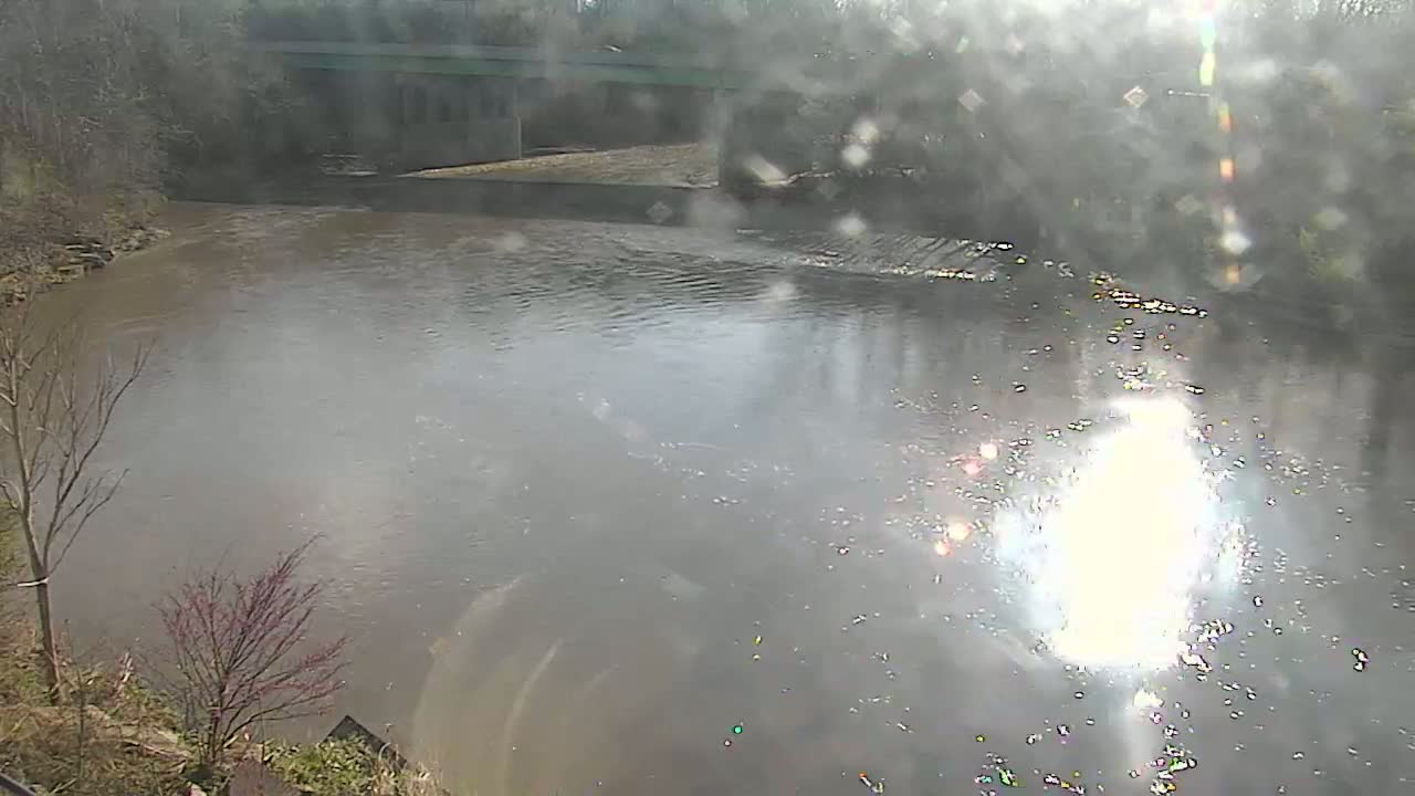 A murky river flows under a bridge on a bright, slightly hazy day.