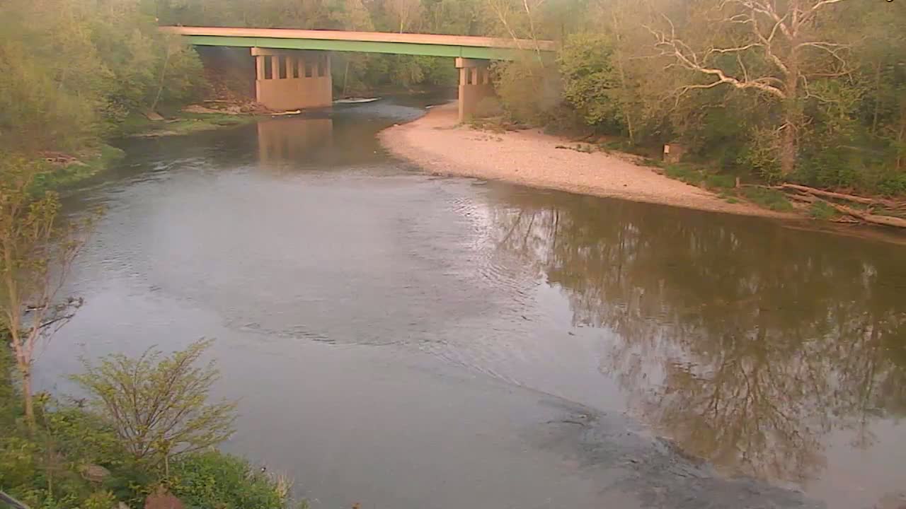 A calm river reflects the trees and a bridge on a hazy day.