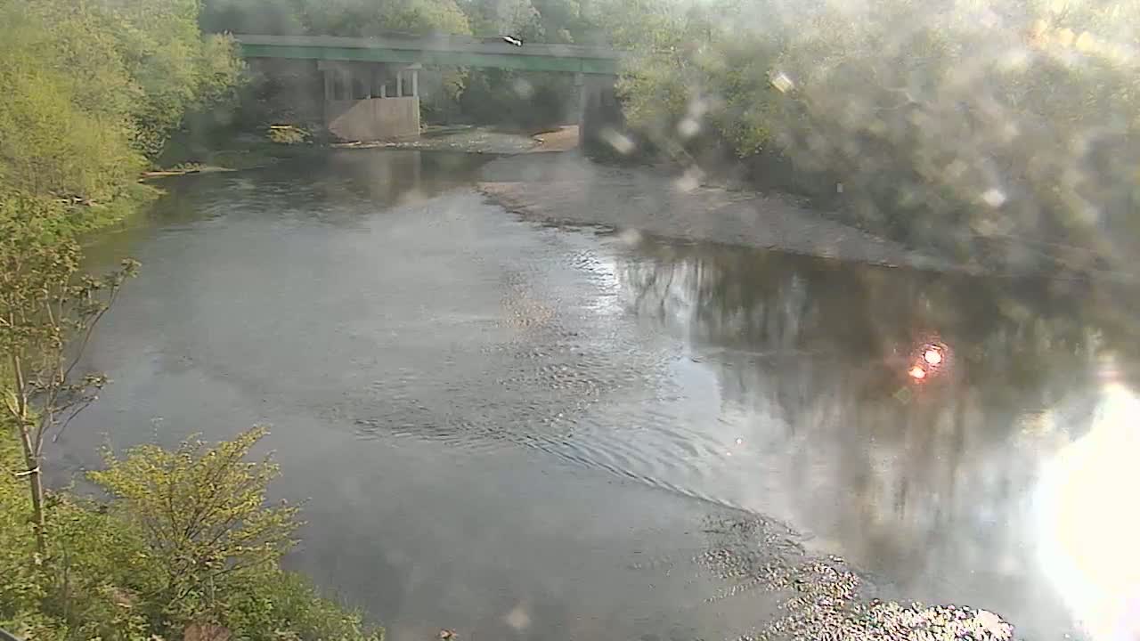 A river flows under a bridge, partially obscured by an overcast sky and a rain-spattered lens.