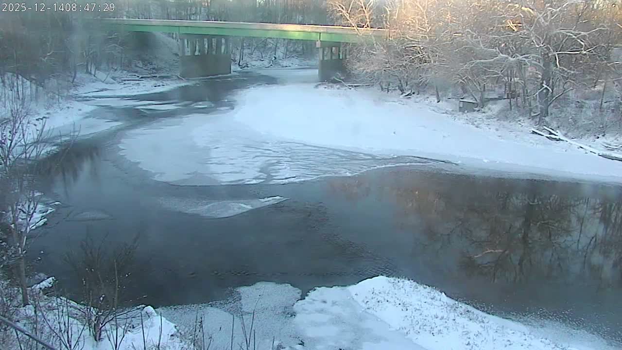A monochrome nighttime image captures a winding river partially frozen with snow-covered banks, illuminated by scattered artificial lights under clear, cold conditions.