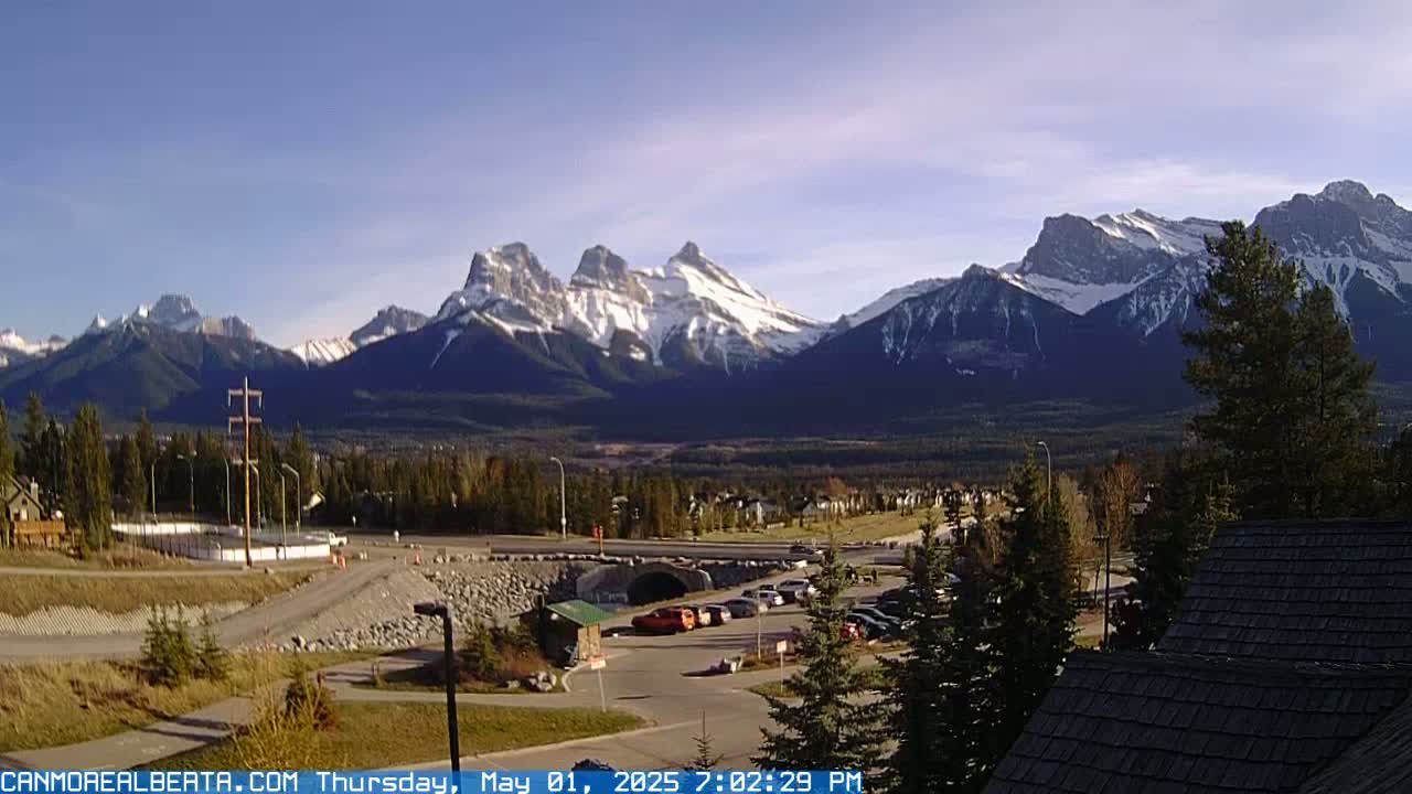 A sunny view of snow-capped mountains in the distance, overlooking a valley with a parking lot, road, and residential area.