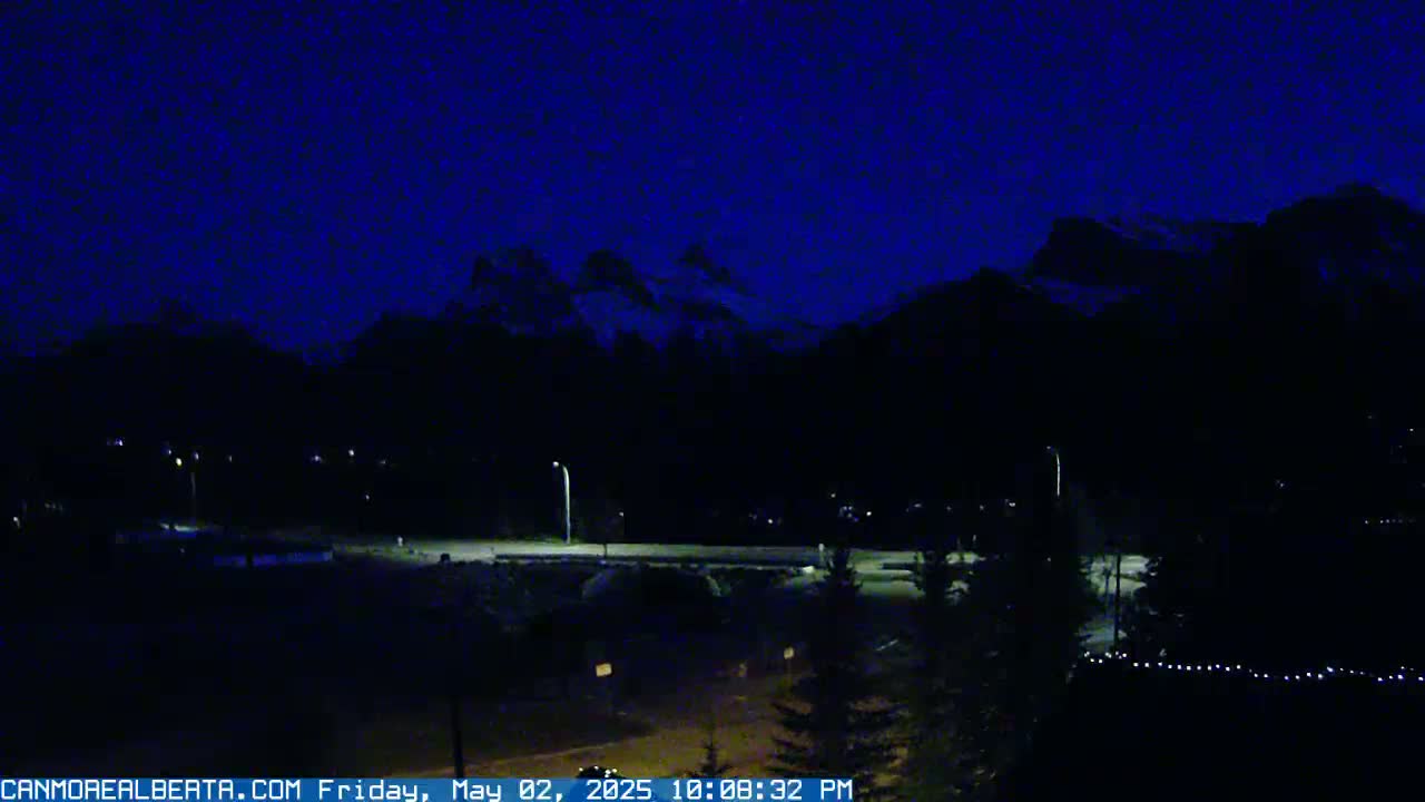A dark nighttime scene shows mountains silhouetted against a deep blue sky, with a road and sparse lights visible below.