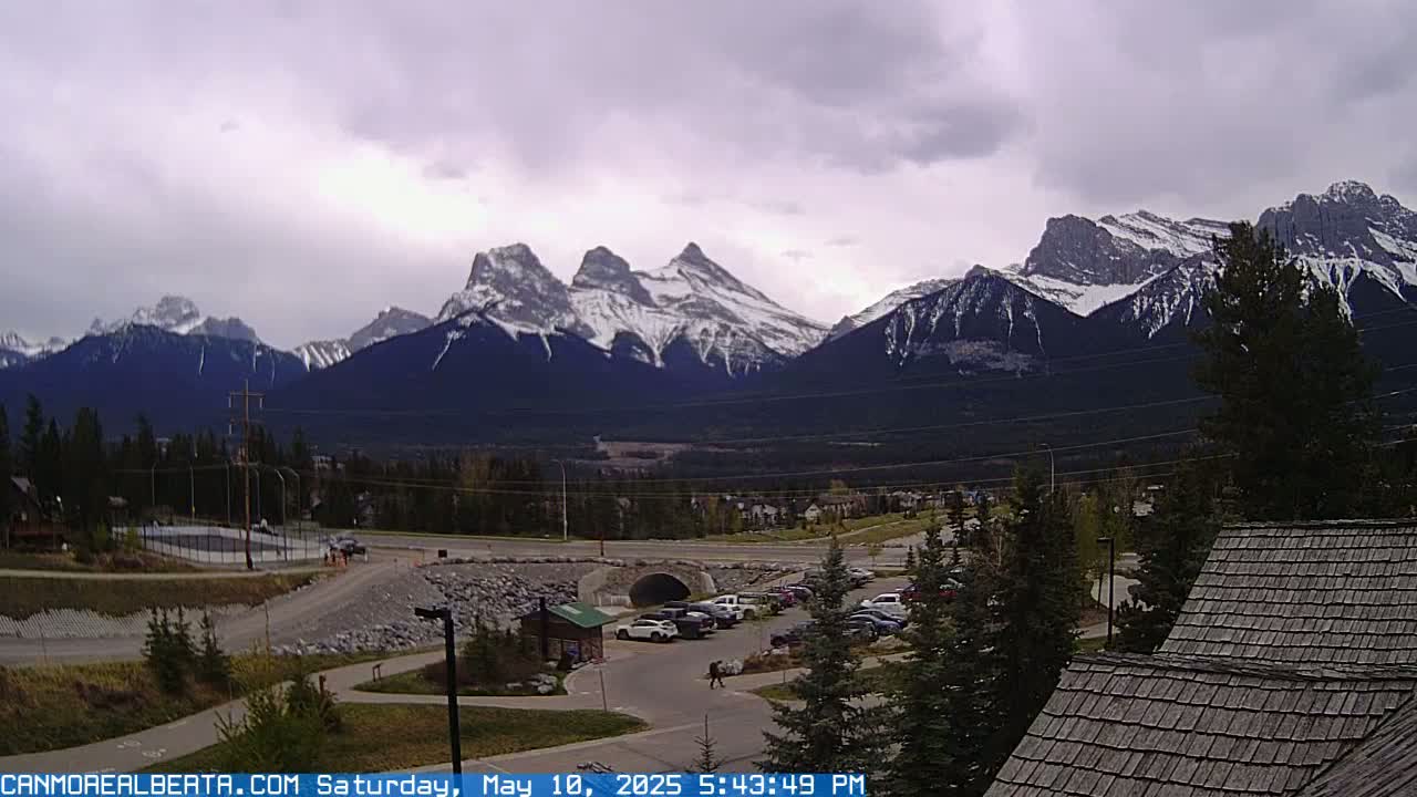 A parking lot and roadway are situated in front of snow-capped mountains under an overcast sky.