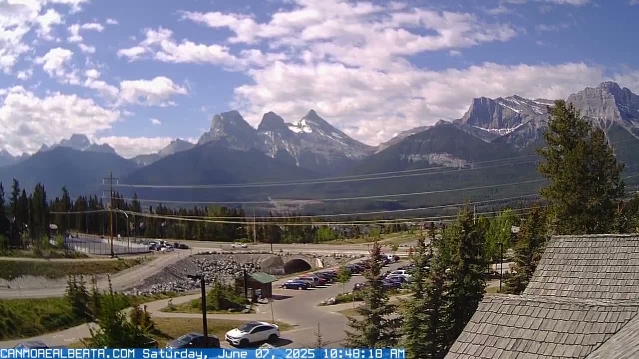 A partly cloudy day reveals a mountain range in the background, with a parking lot and roadway visible in the foreground.