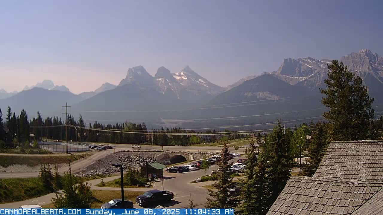 A clear, hazy day reveals a mountain range in the distance, with a parking lot, roadway, and some buildings in the foreground.
