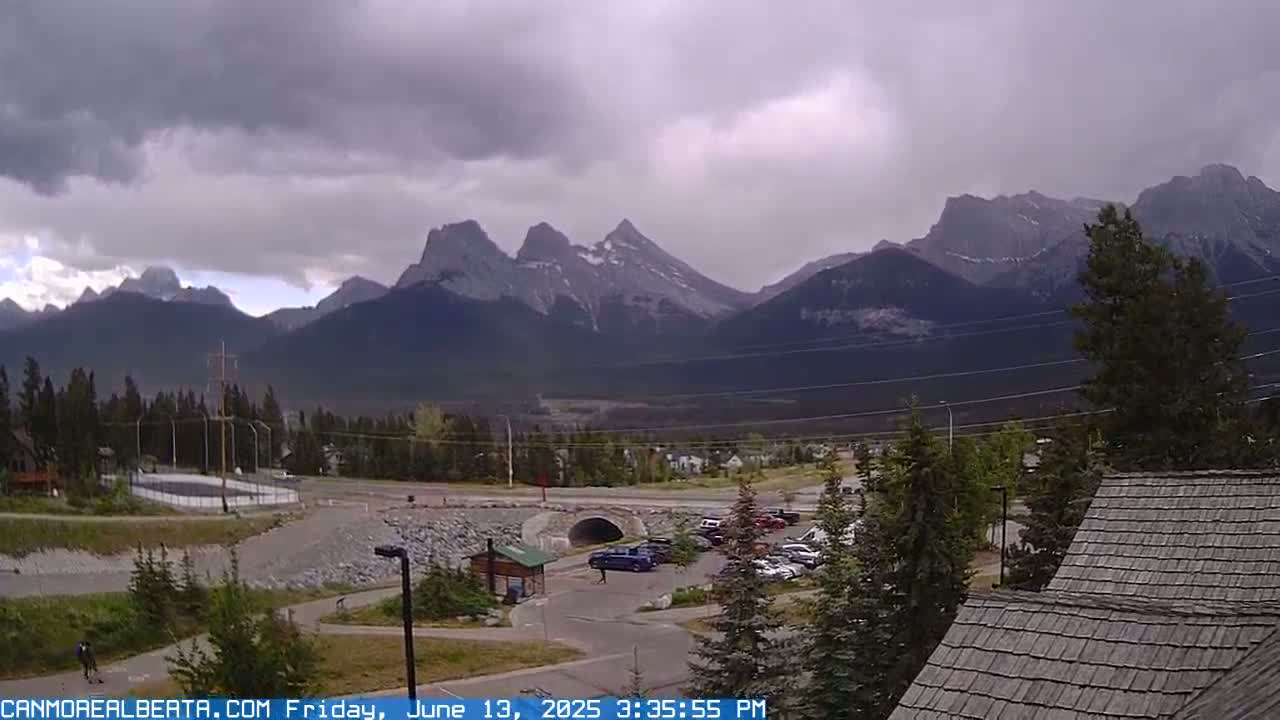 A parking lot and a small town sit before a large mountain range under a cloudy sky.