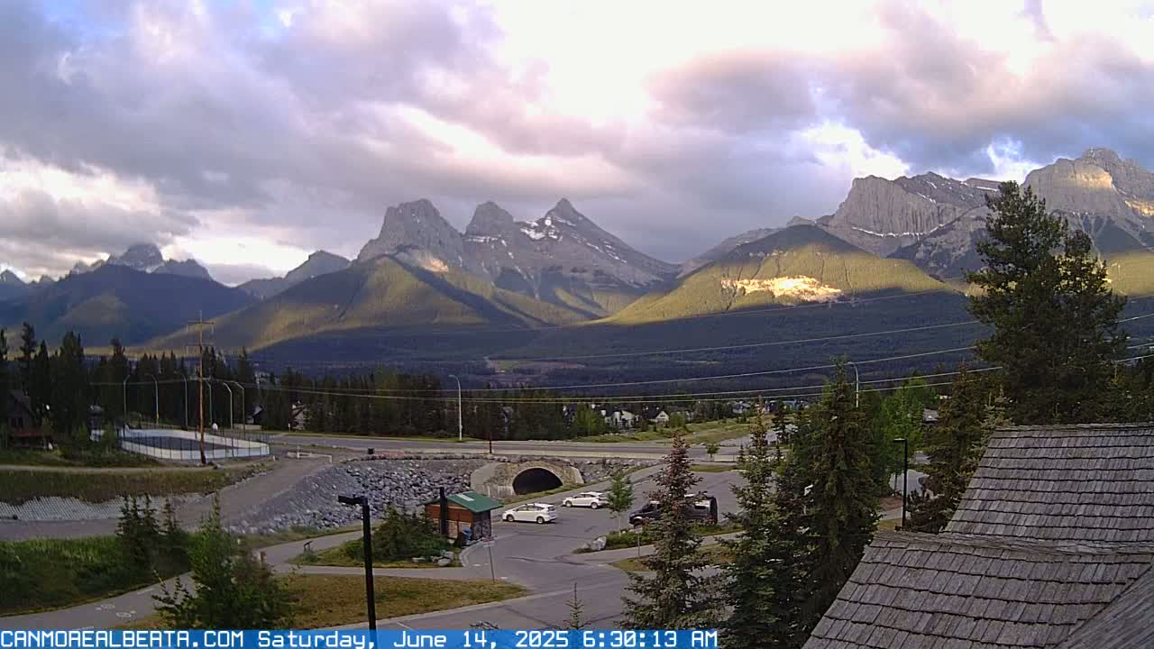 A partly cloudy sunrise illuminates a mountain range overlooking a parking lot and residential area.