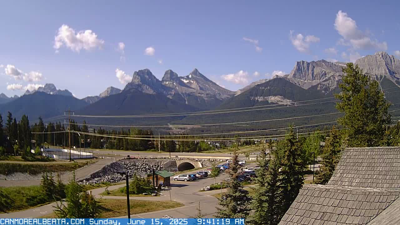 A sunny day with a few clouds shows a mountain range in the background, a parking lot, and a roadway in the foreground.