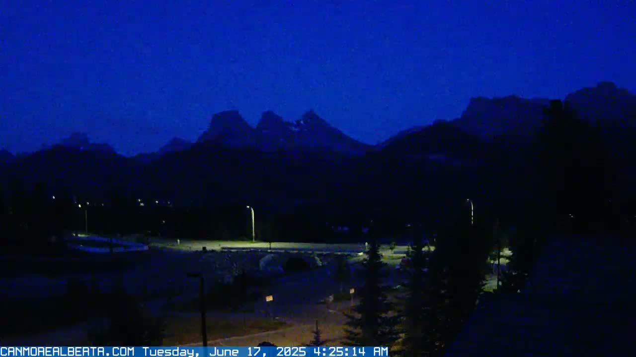 A dark, pre-dawn view of a town nestled at the base of a mountain range under a clear, deep blue sky.