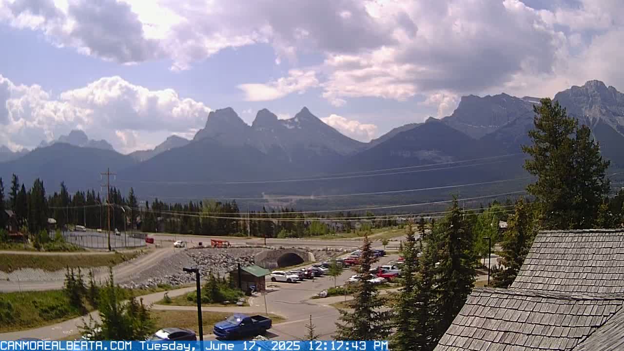 A partly cloudy day reveals a mountain range in the distance, with a parking lot and a roadway in the foreground.