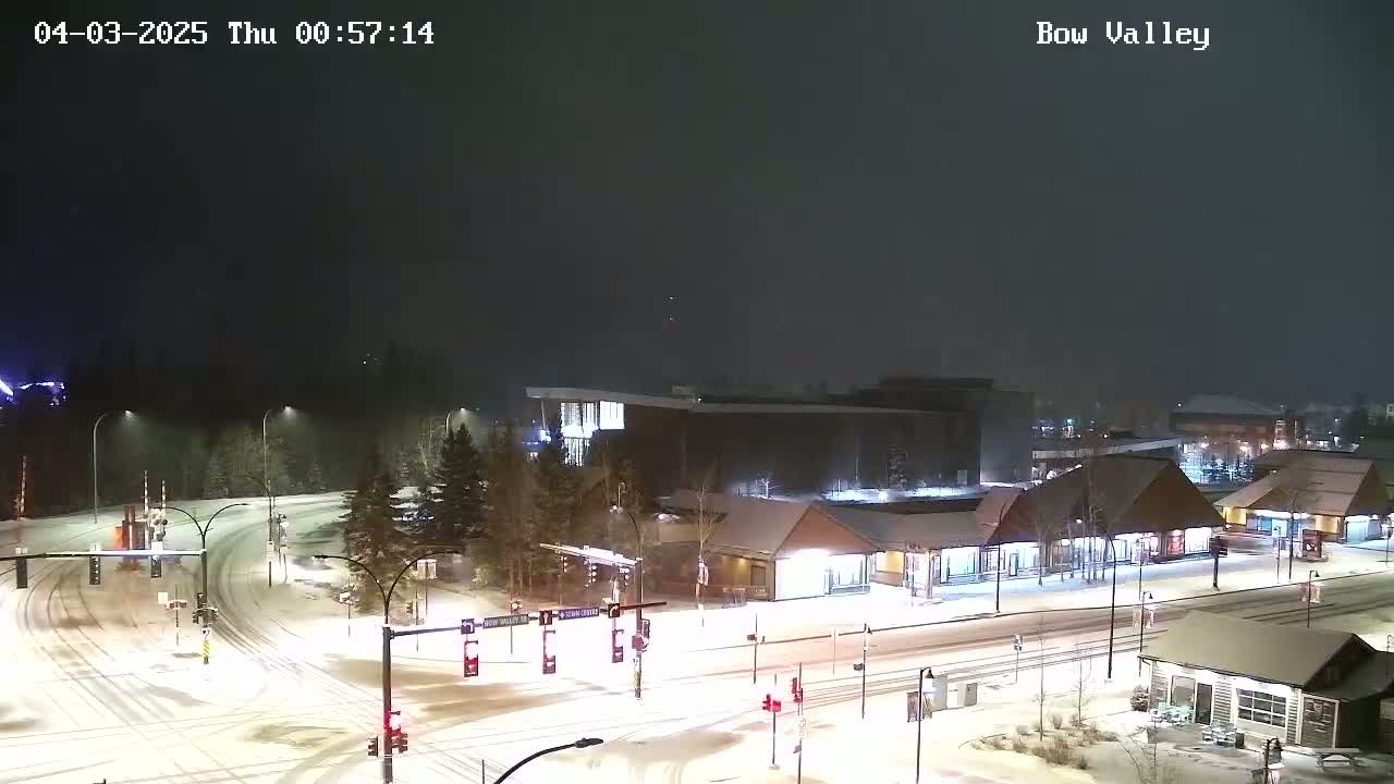 A snow-covered intersection and surrounding buildings are visible at night, under light snowfall.