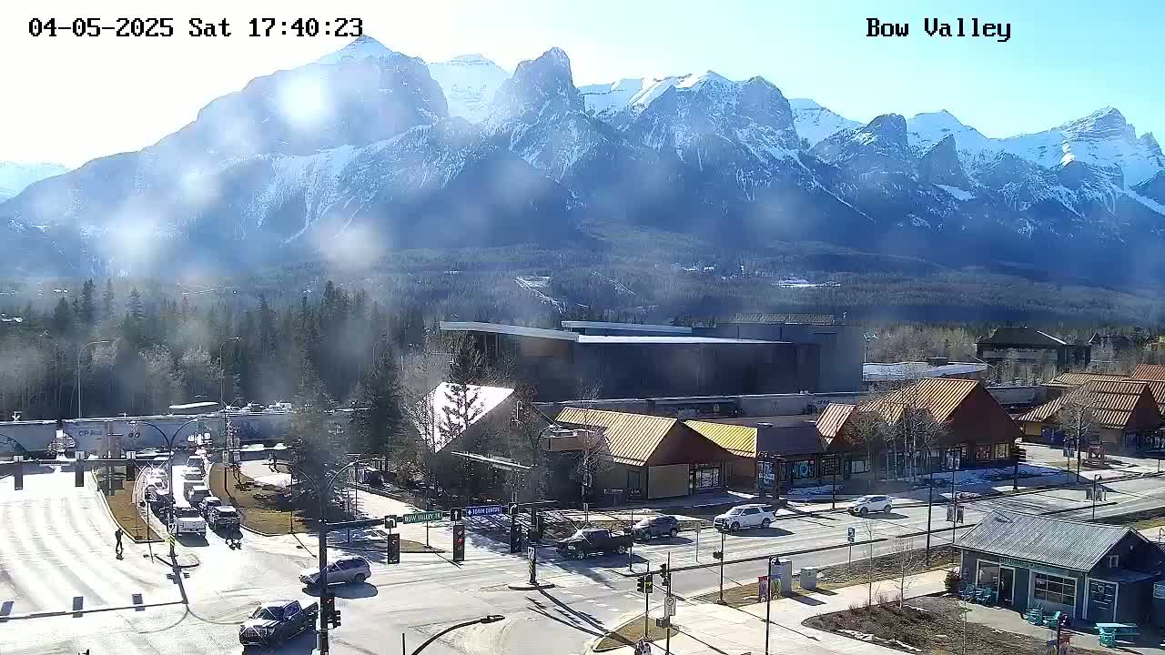 A hazy, sunny day reveals a mountain range behind a town with buildings and cars at an intersection.