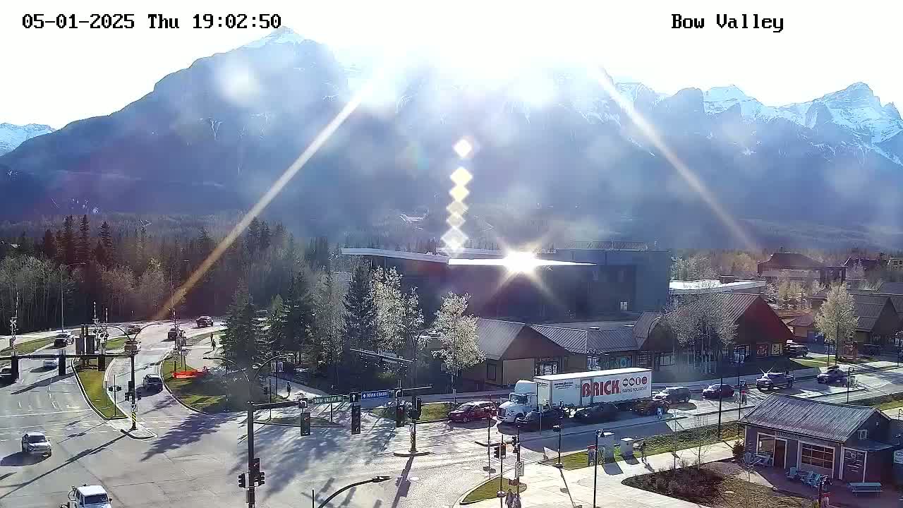 A sunny day reveals a mountain range in the background of a valley town with vehicles at an intersection.
