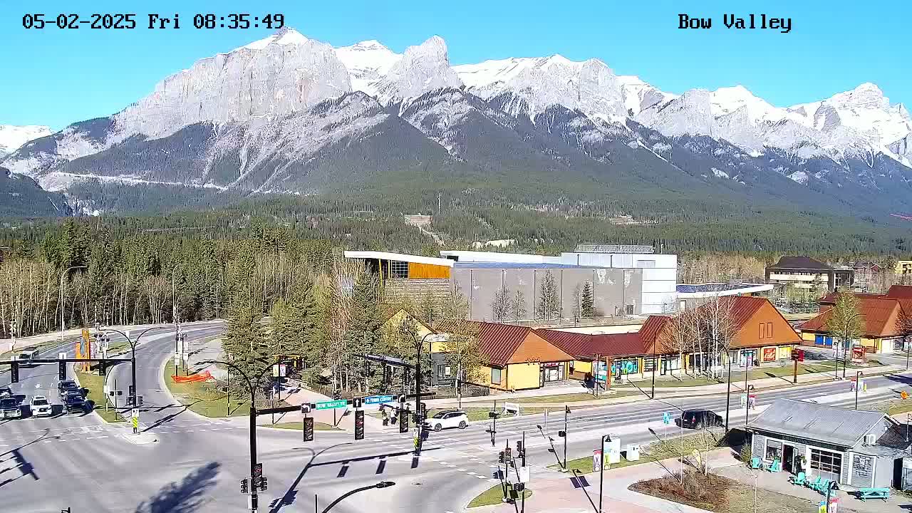 A sunny day reveals a mountain range covered in snow, overlooking a town with a crossroads and various buildings, including shops and a larger structure.
