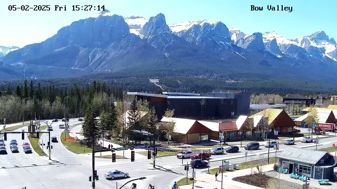 A sunny day reveals a mountain range in the background, with a town featuring roads, buildings, and cars in the foreground.