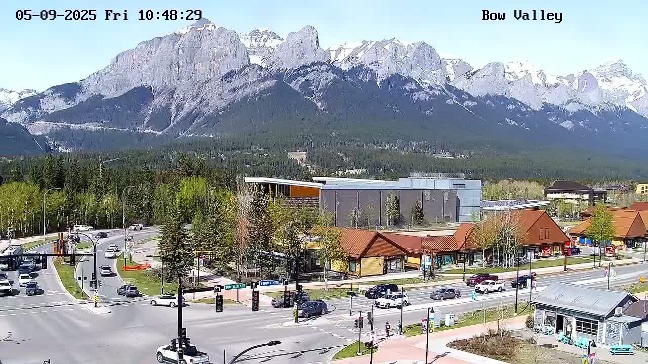A sunny view of a mountain range overlooking a town with shops and roads, featuring several vehicles.