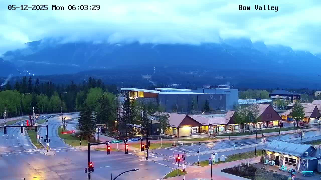 A wet, overcast morning scene shows a mountain range in the background, with a town featuring roads, buildings, and traffic lights in the foreground.