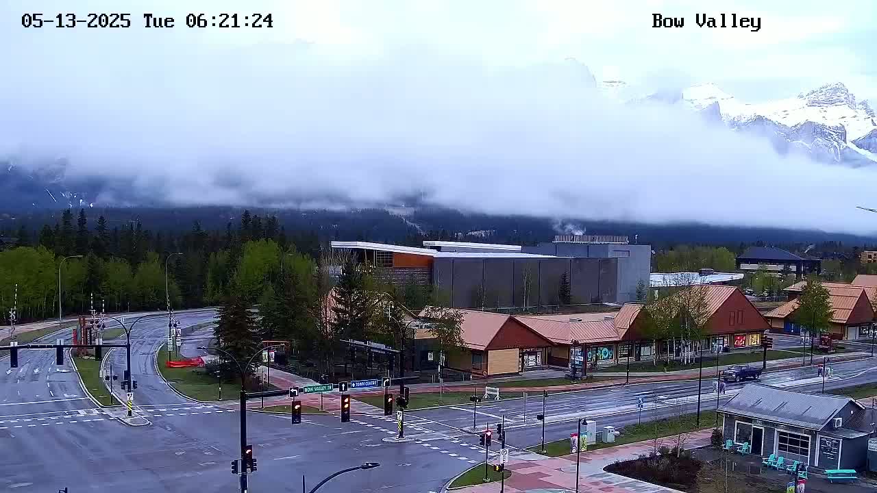 A misty mountain range looms over a town's intersection, where buildings and vehicles are visible on a wet street.