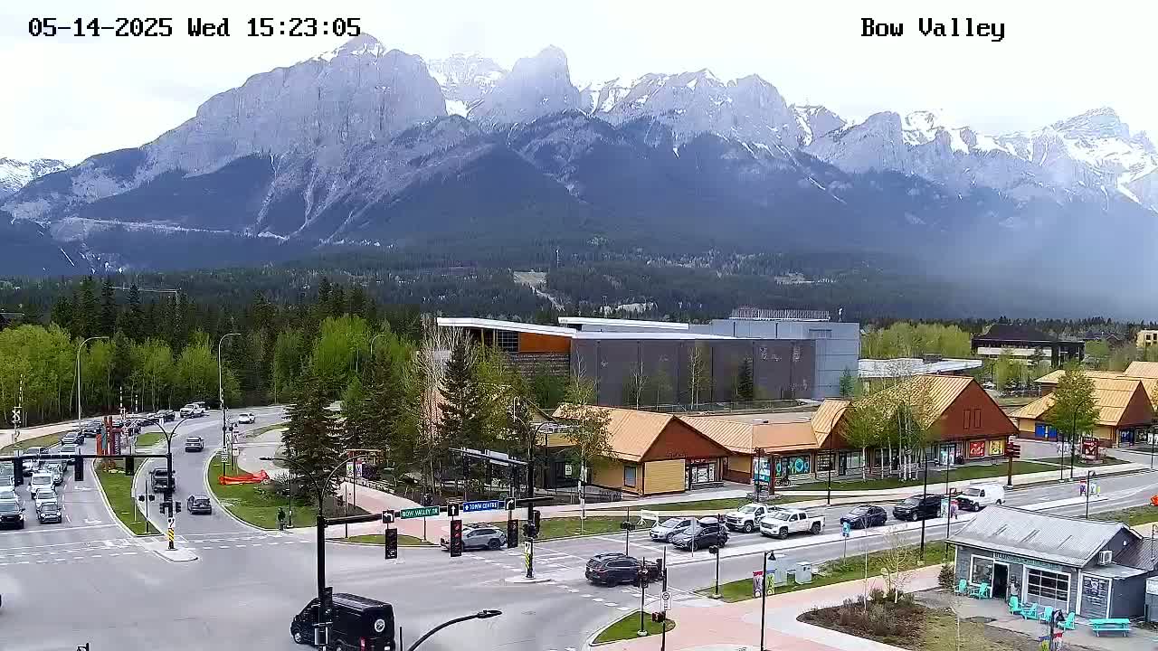 A partly cloudy day shows a mountain range in the background behind a town with a few cars on the roads.