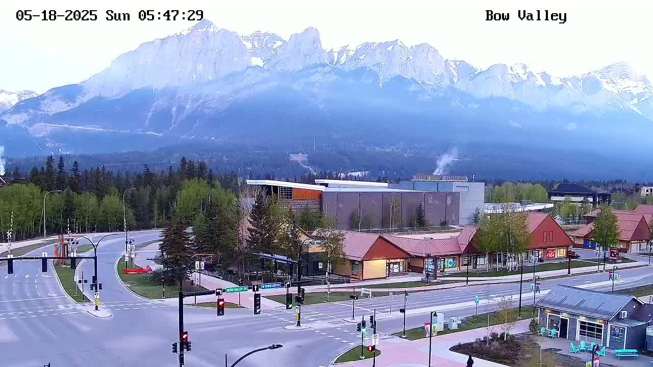 A hazy mountain range is visible in the background of a town's street intersection with several buildings, including shops and a larger structure.