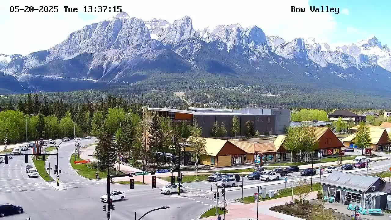 A sunny day reveals a mountain range in the background of a town scene with roads, buildings, and cars.