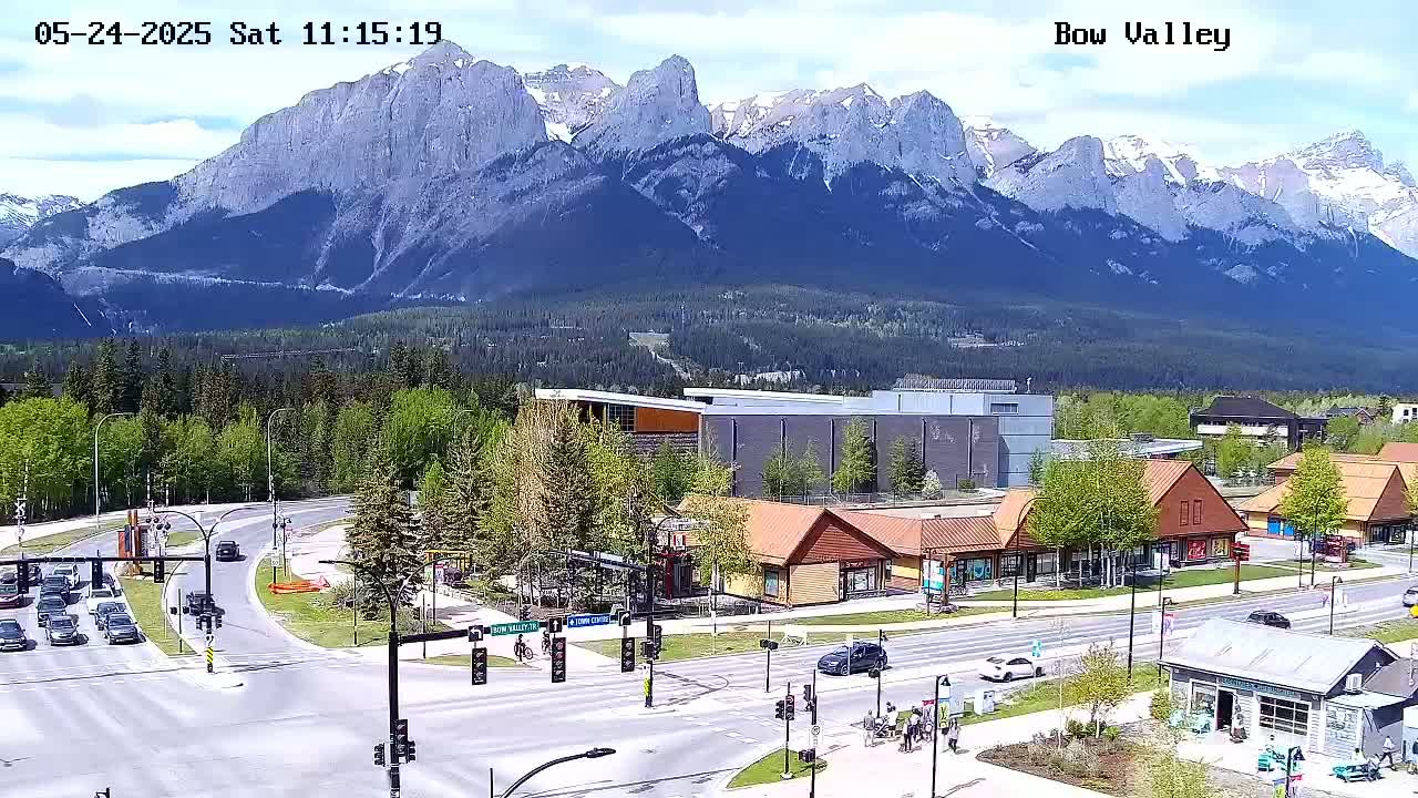 A partly cloudy day reveals a mountain range in the background overlooking a town square with buildings and traffic.