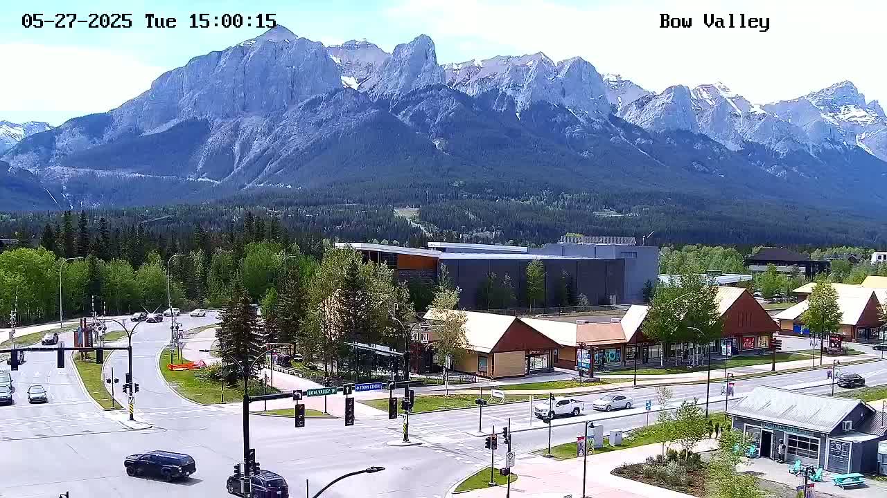 A mountain range under a clear sky overlooks a town's roads and buildings, with cars driving along streets.