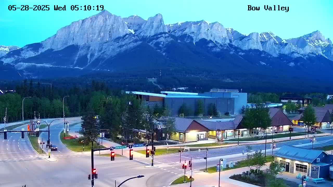 A mountain range is visible in the background under a twilight sky, overlooking a town with buildings, roads, and traffic lights.